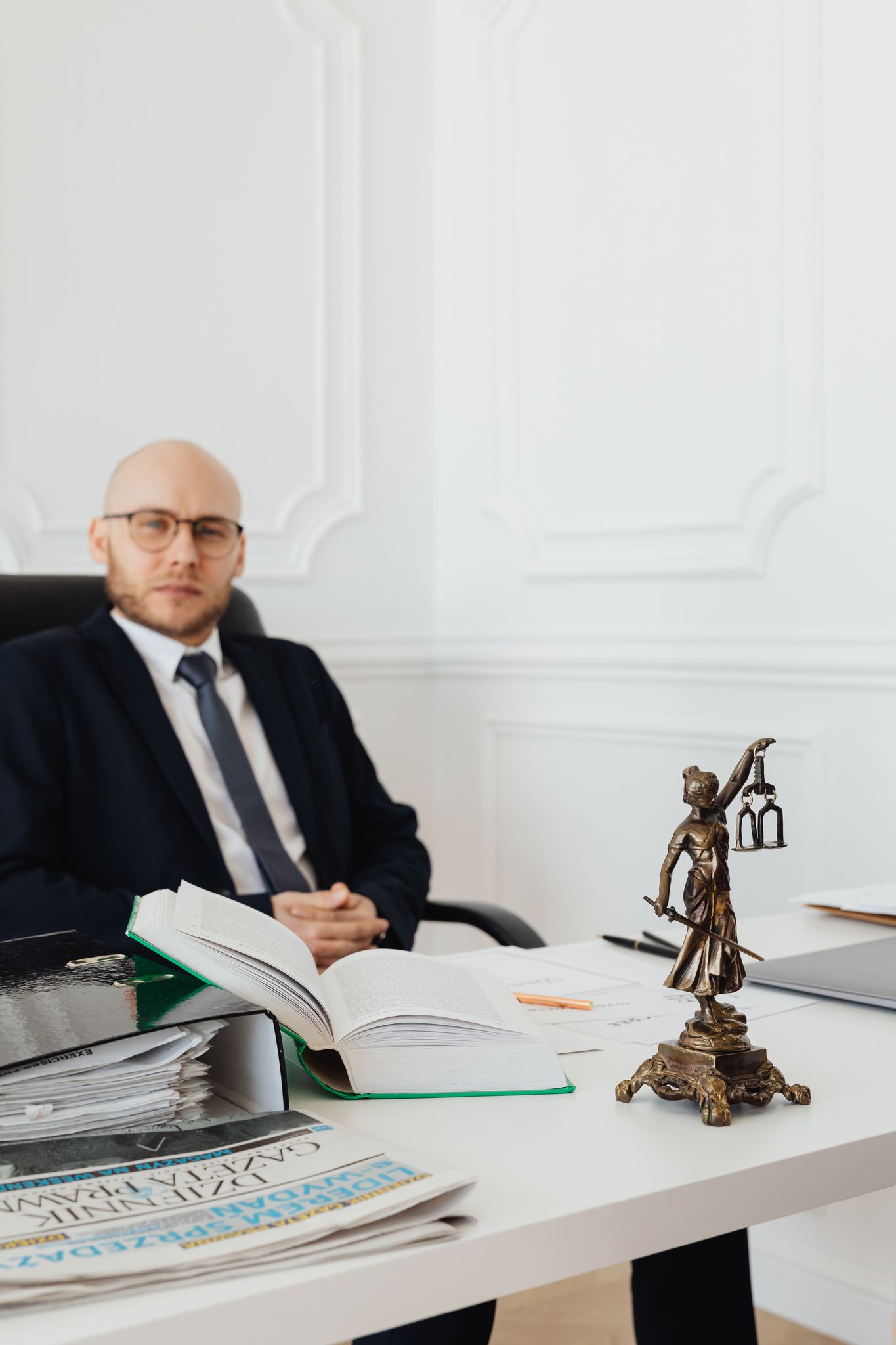A lawyer in a suit sitting at a desk with legal books and Lady Justice statue.